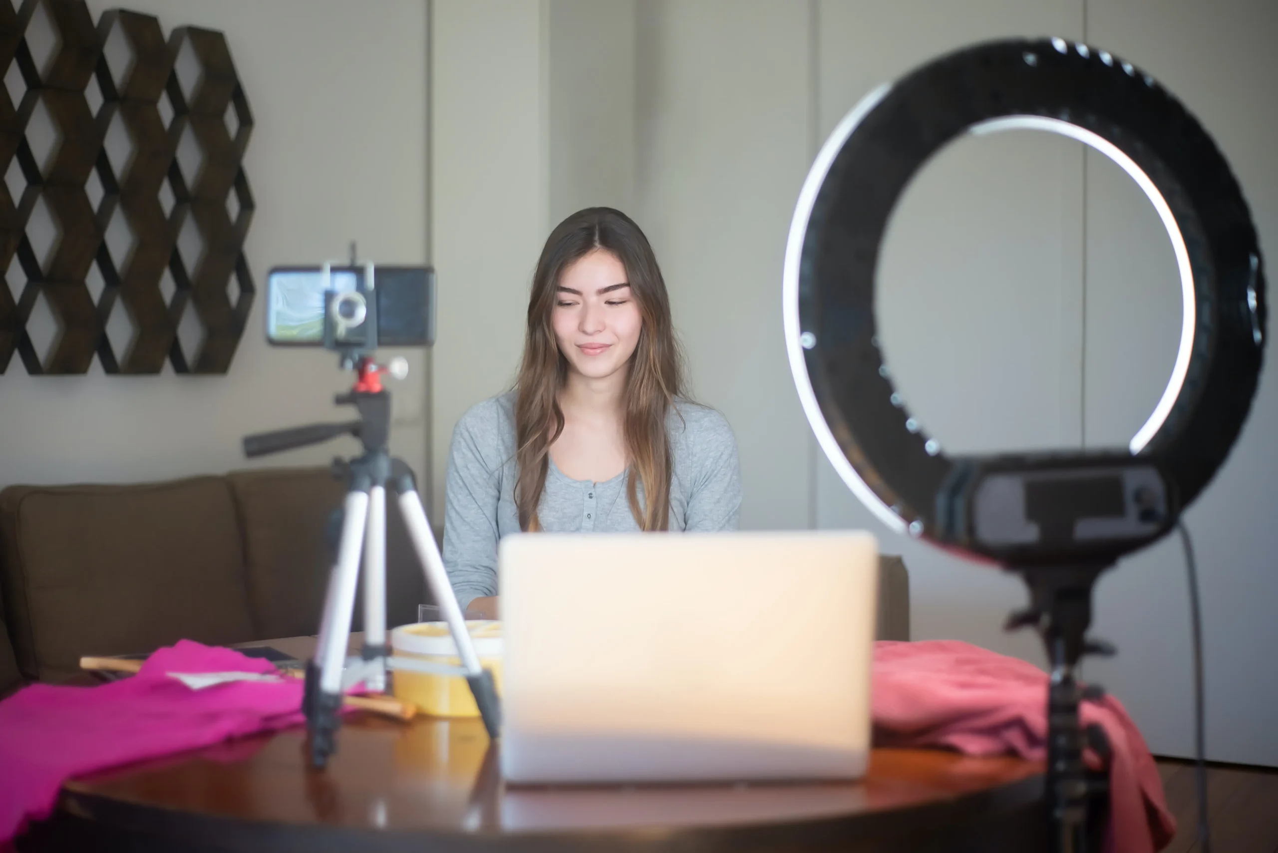 This image describes an Influencer doing vlogging with a smartphone camera, a ring light and a laptop in front of her.